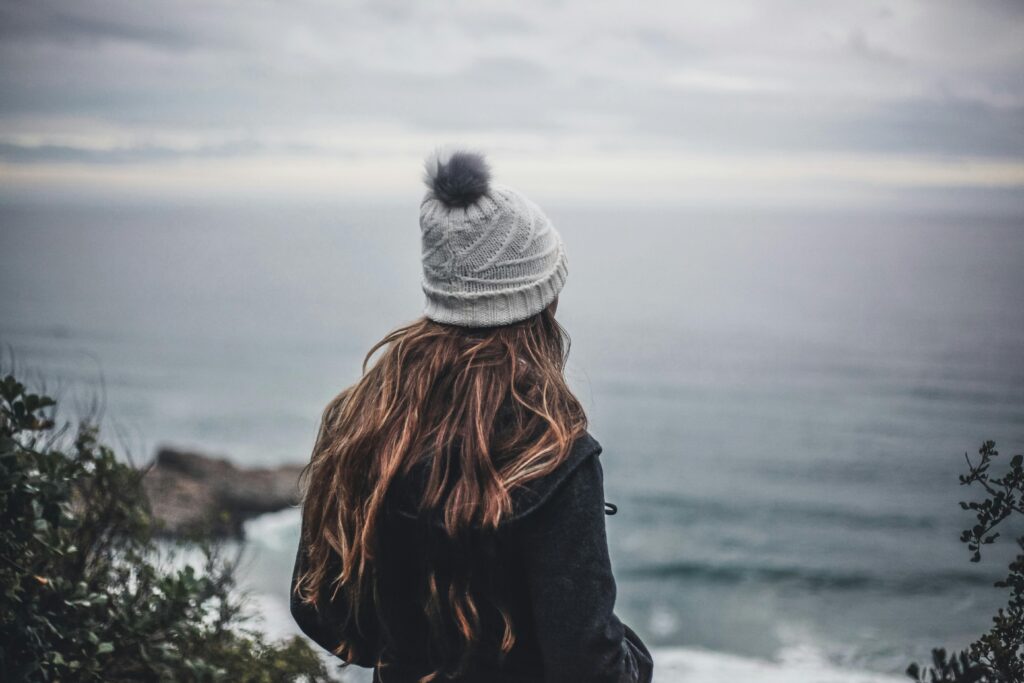 My personal finance journey (very abbreviated) A woman in a beanie gazes at the open sea, embodying quiet contemplation and nature's beauty.